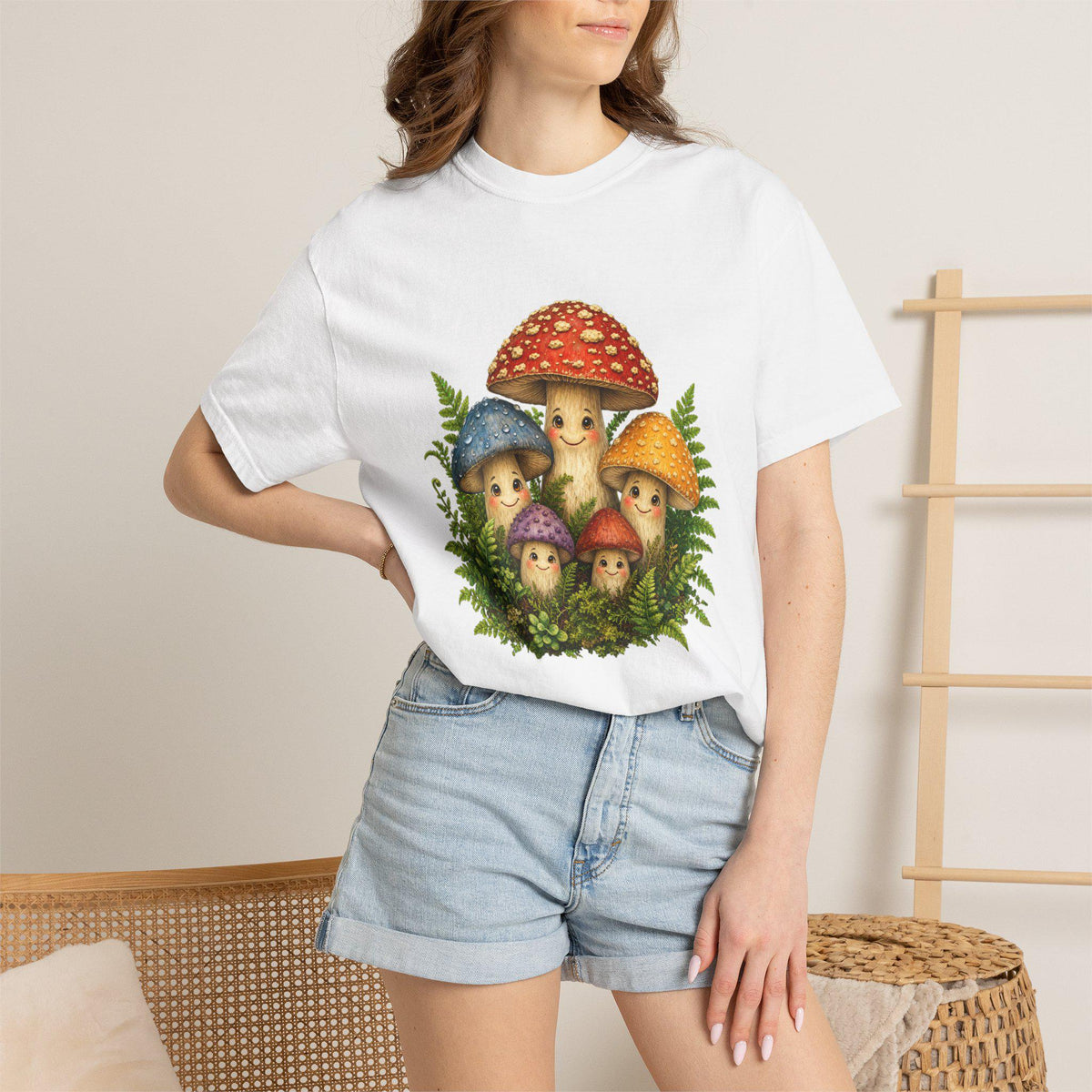A person wearing a white t-shirt with a graphic of five smiling mushrooms and green ferns, paired with denim shorts.