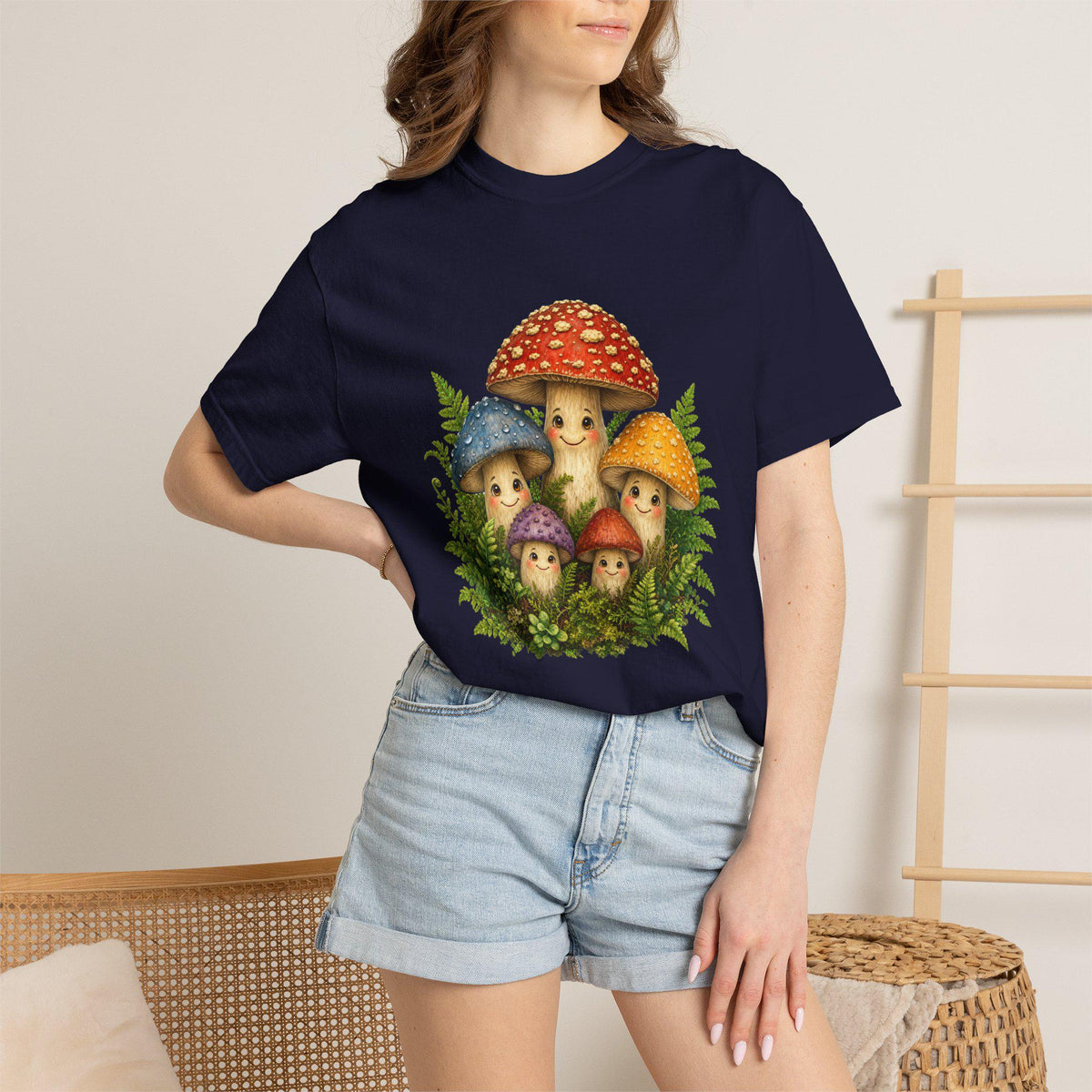 A person wearing a navy blue t-shirt with a graphic of five smiling mushrooms and green ferns, paired with denim shorts.