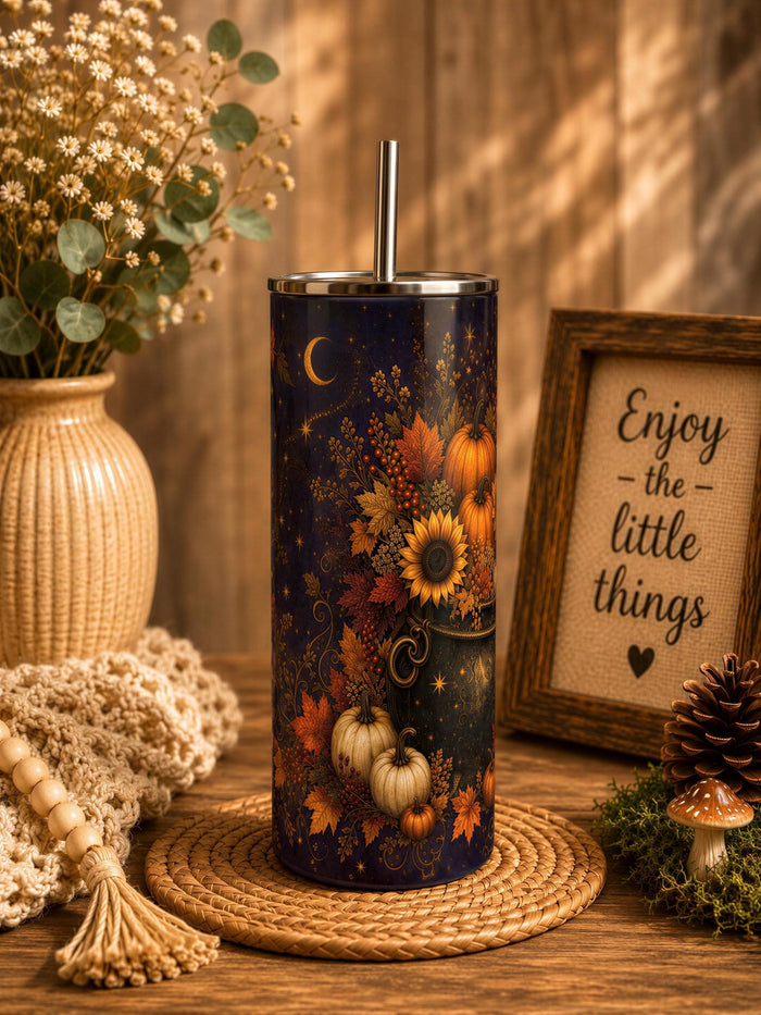 a tall, cylindrical container with a pumpkin and flower design on it, placed on a woven mat. The container has a straw sticking out of the top. The setting includes a framed picture, a vase with flowers, and a tassel. The background appears to be a wooden surface with a rustic, autumnal theme.