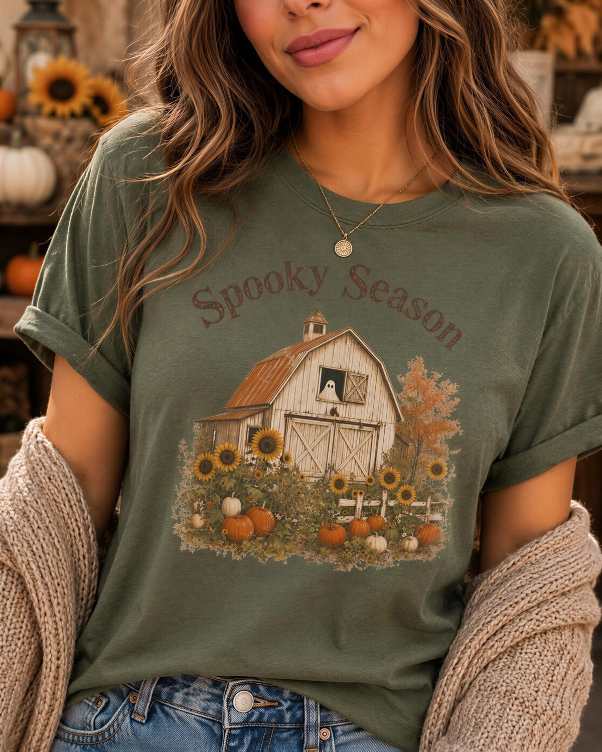 A woman wearing a green t-shirt with a graphic of a barn and autumn foliage, along with the text "Spooky Season".