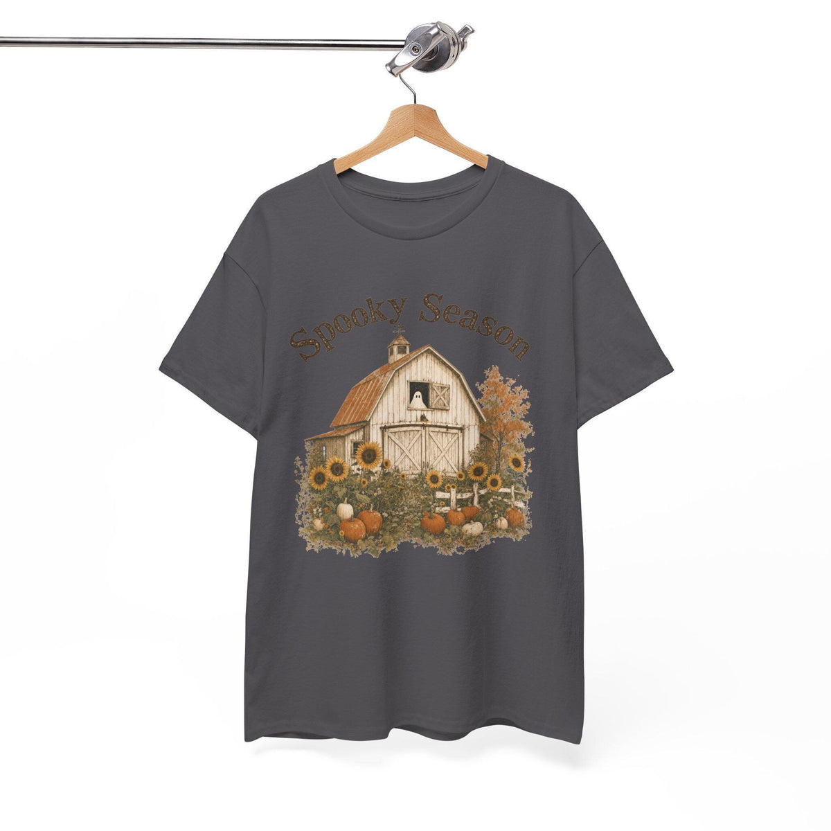 A dark gray t-shirt hanging on a wooden hanger, displaying a graphic of a white barn, sunflowers, and pumpkins, with "Spooky Season" text above.